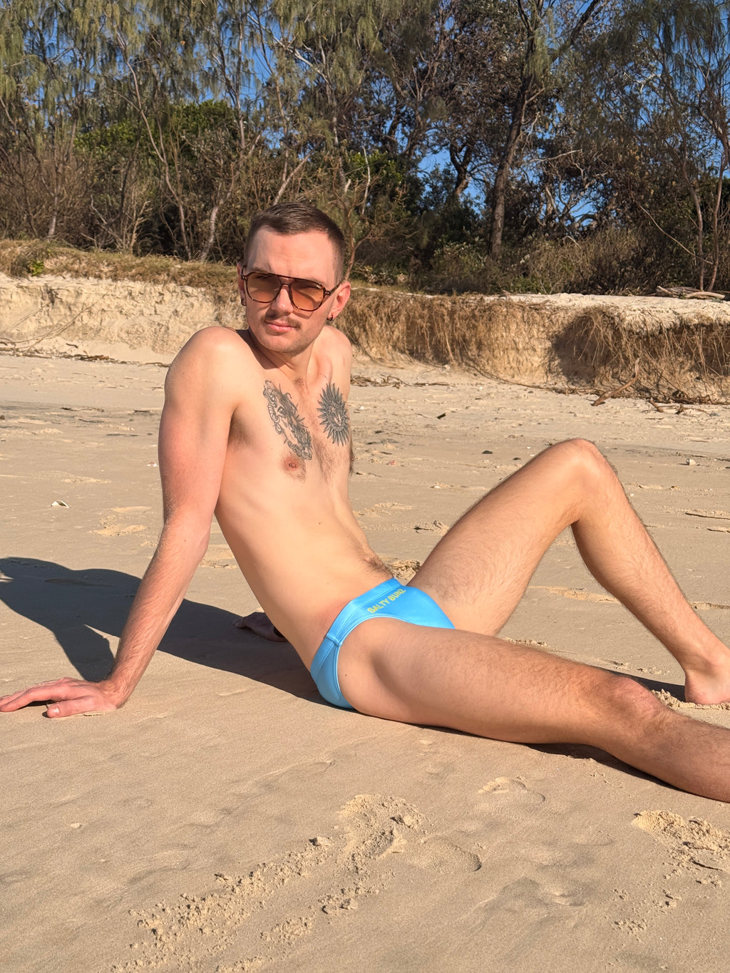 Salty Bunz Bikini Swim Brief Ultra-Thin 3.5cm Ocean Oasis Sky Blue with beach dunes trees background 2 right side Gay swimwear Model Scott