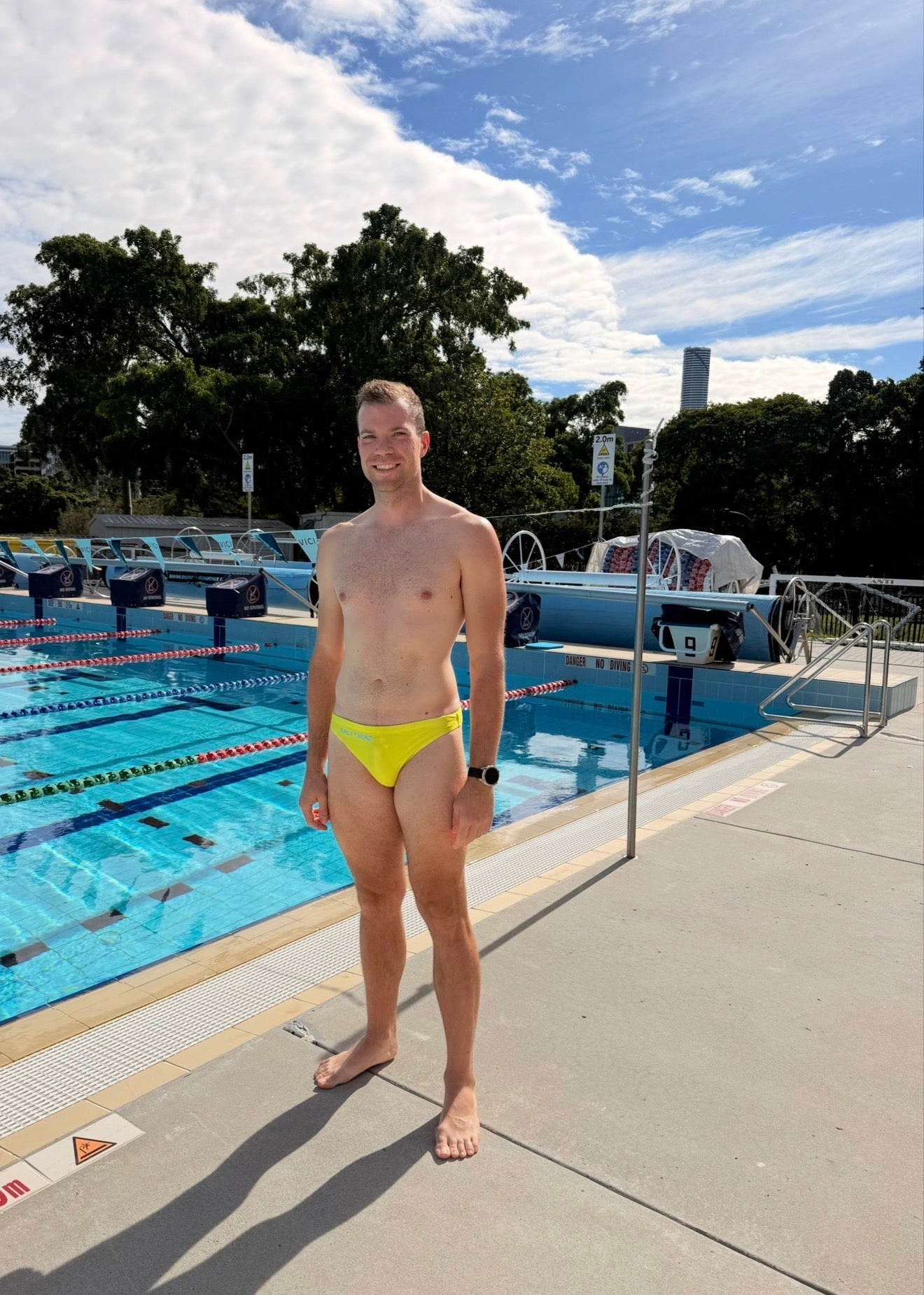 Salty Bunz Bikini Swim Brief Ultra-Thin 3.5cm Citrus Current Yellow with competition pool background front Gay swimwear Model Jonas